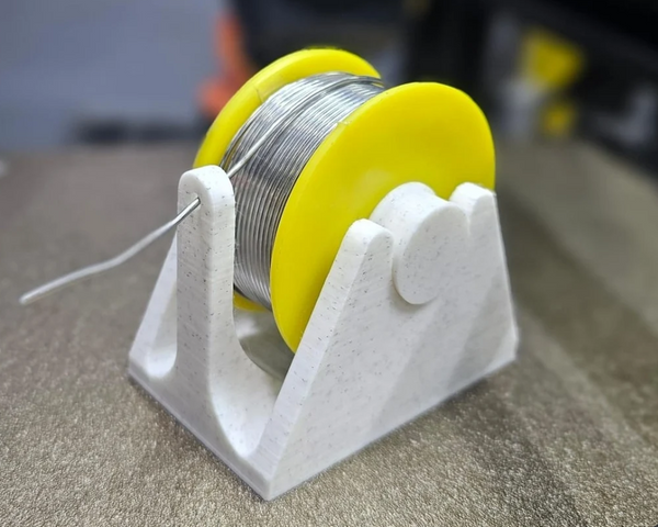 A white 3D-printed stand holding a spool of silver solder wire with yellow end caps, designed for easy solder dispensing.