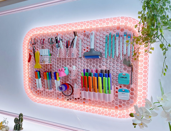 A wall-mounted 3D-printed honeycomb storage panel with LED lighting around the edges, holding various office supplies and stationery items.