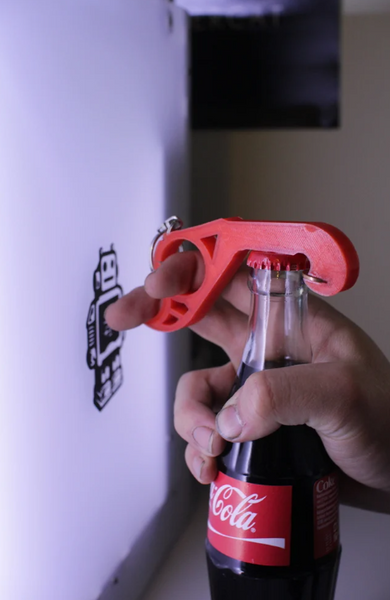 A red 3D-printed bottle opener designed for one-handed use, shown opening a glass bottle with ease.