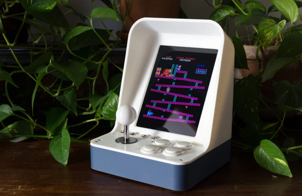 A mini 3D-printed retro-style arcade cabinet with a small screen and joystick, featuring a classic arcade game on display.