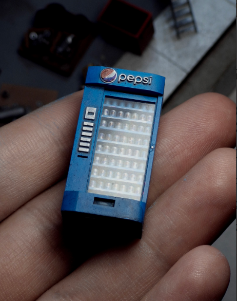 A miniature 3D-printed Pepsi vending machine, held in hand, with fine details perfect for garage dioramas.