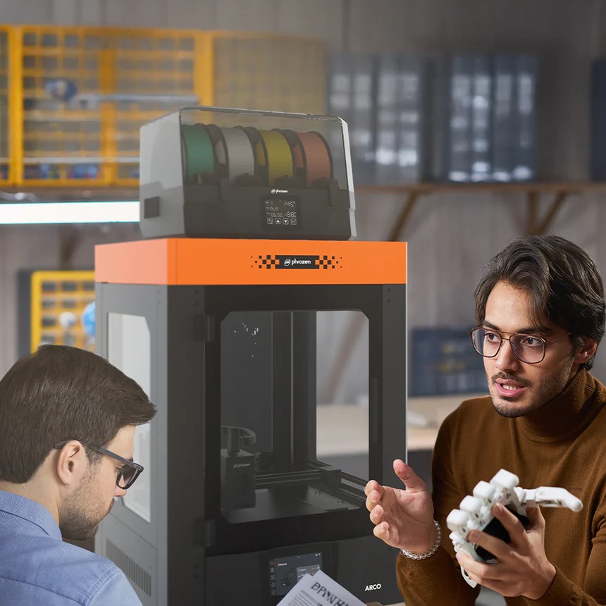 Two designers review a white prototype beside an ARCO 3D printer in a studio.